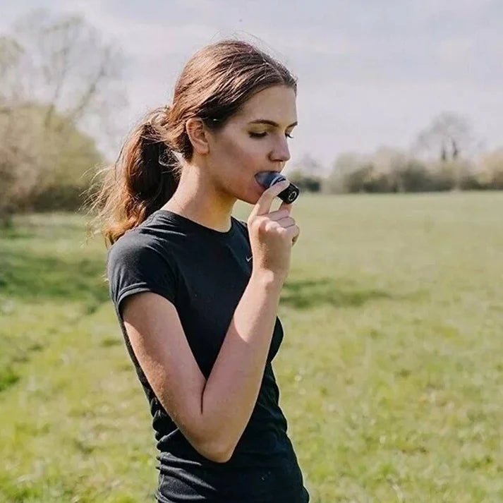 Woman in a black shirt holding a black object outdoors in a field