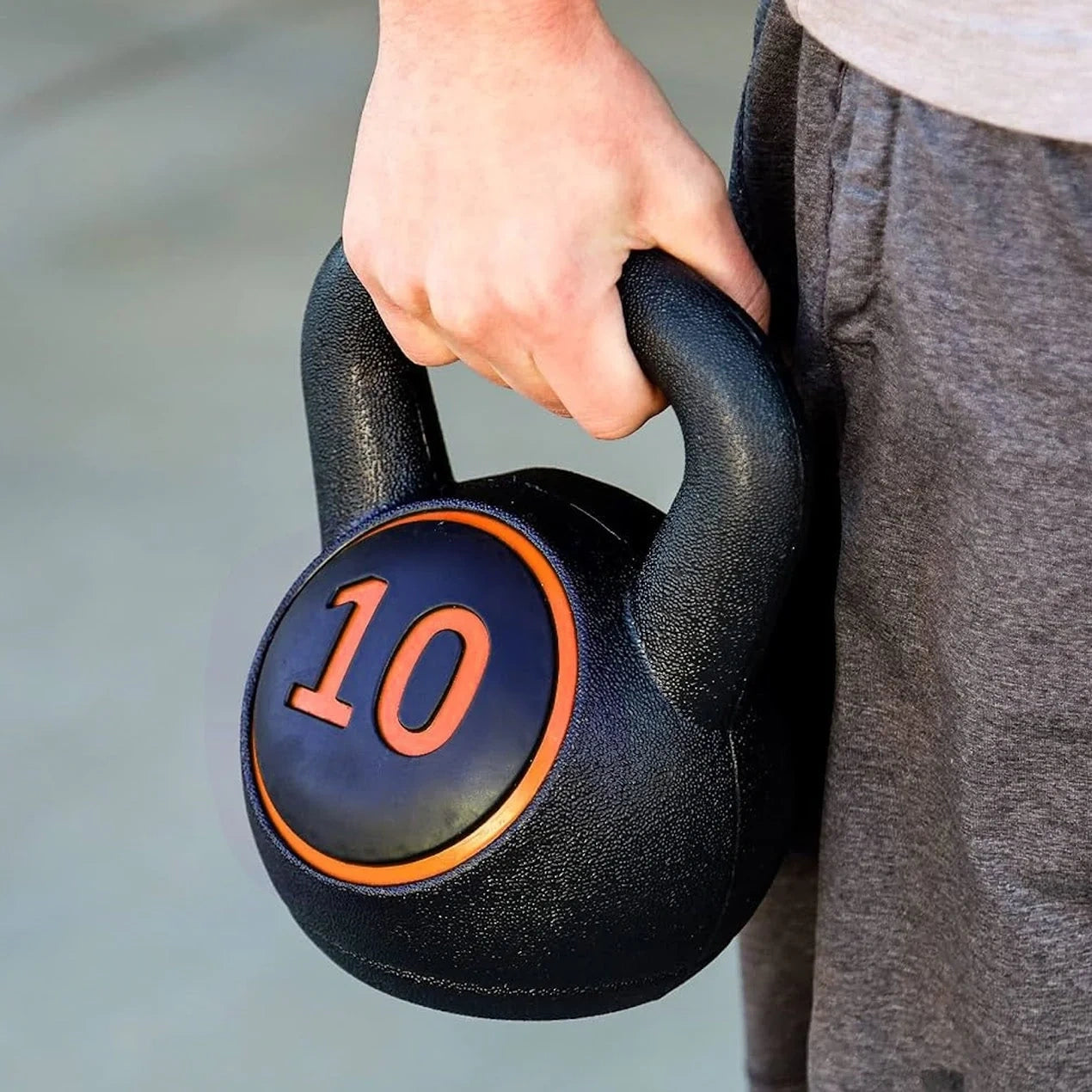 Person holding a black kettlebell with '10' marking on a blurred background